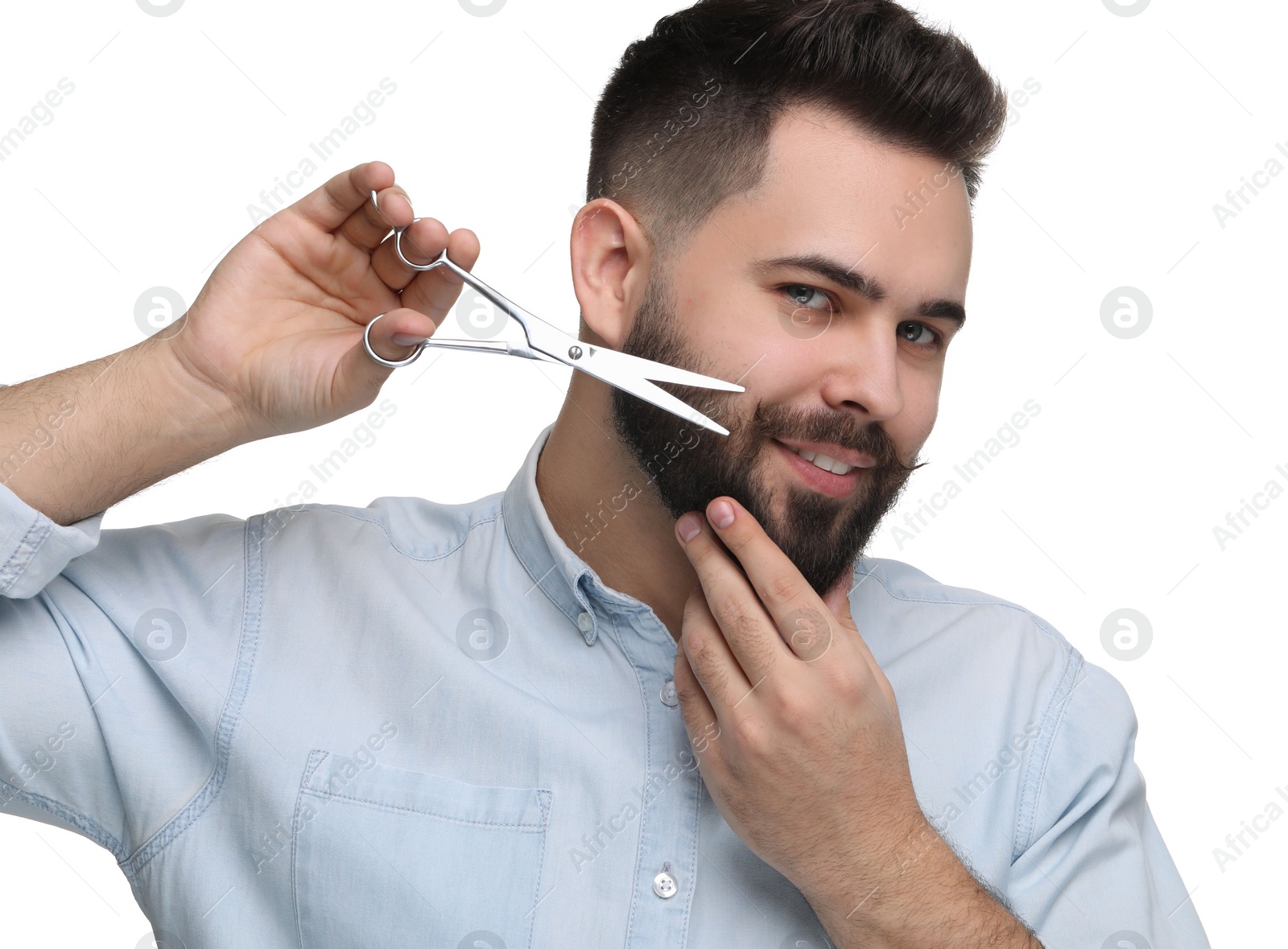 Photo of Handsome young man trimming beard with scissors on white background