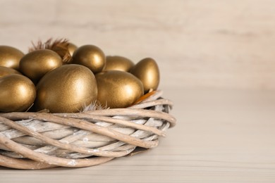 Photo of Golden eggs in nest on white wooden table, closeup. Space for text