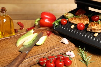 Photo of Electric grill with different products and knife on wooden table