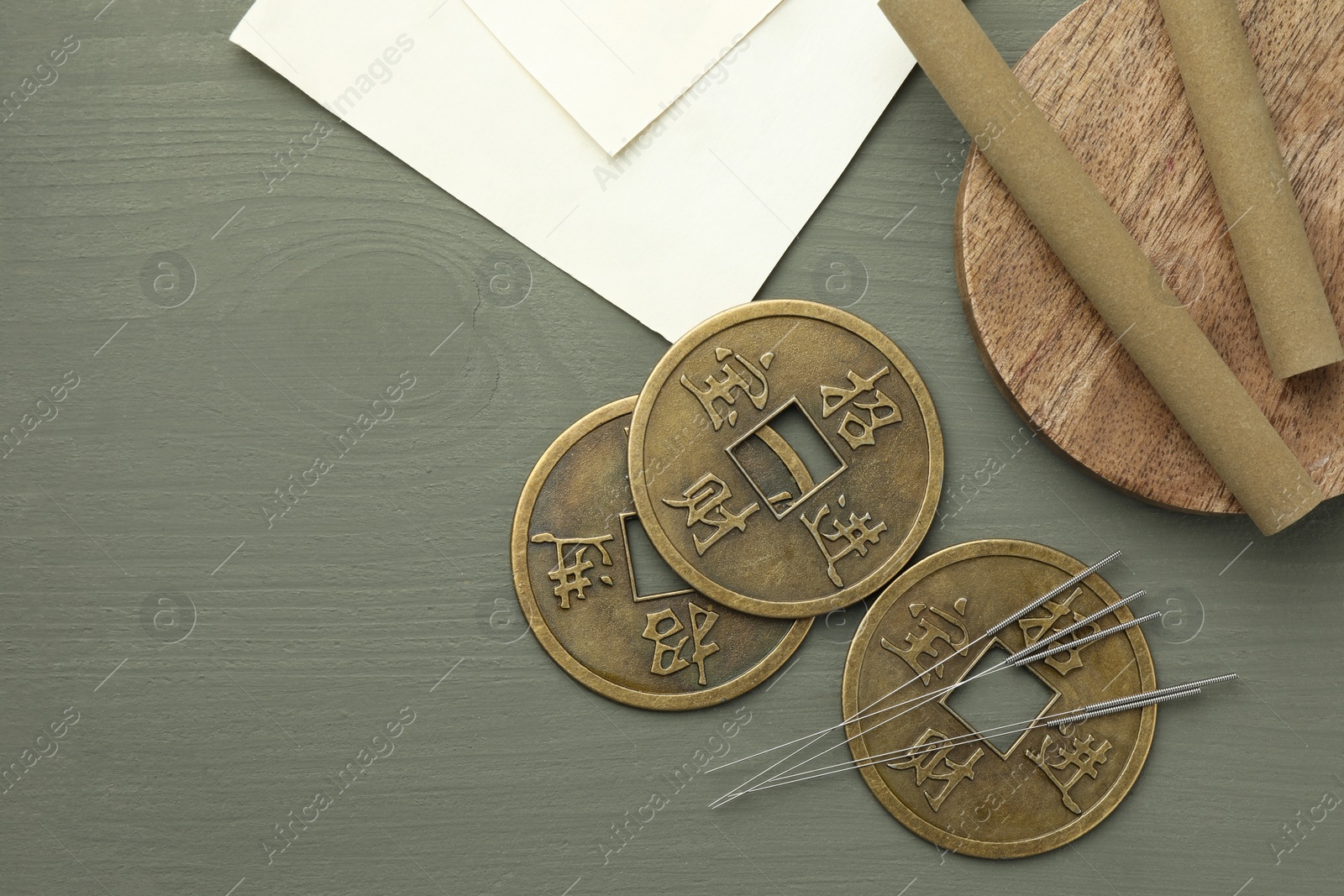 Photo of Acupuncture needles, moxa sticks and antique Chinese coins on grey wooden table, flat lay. Space for text