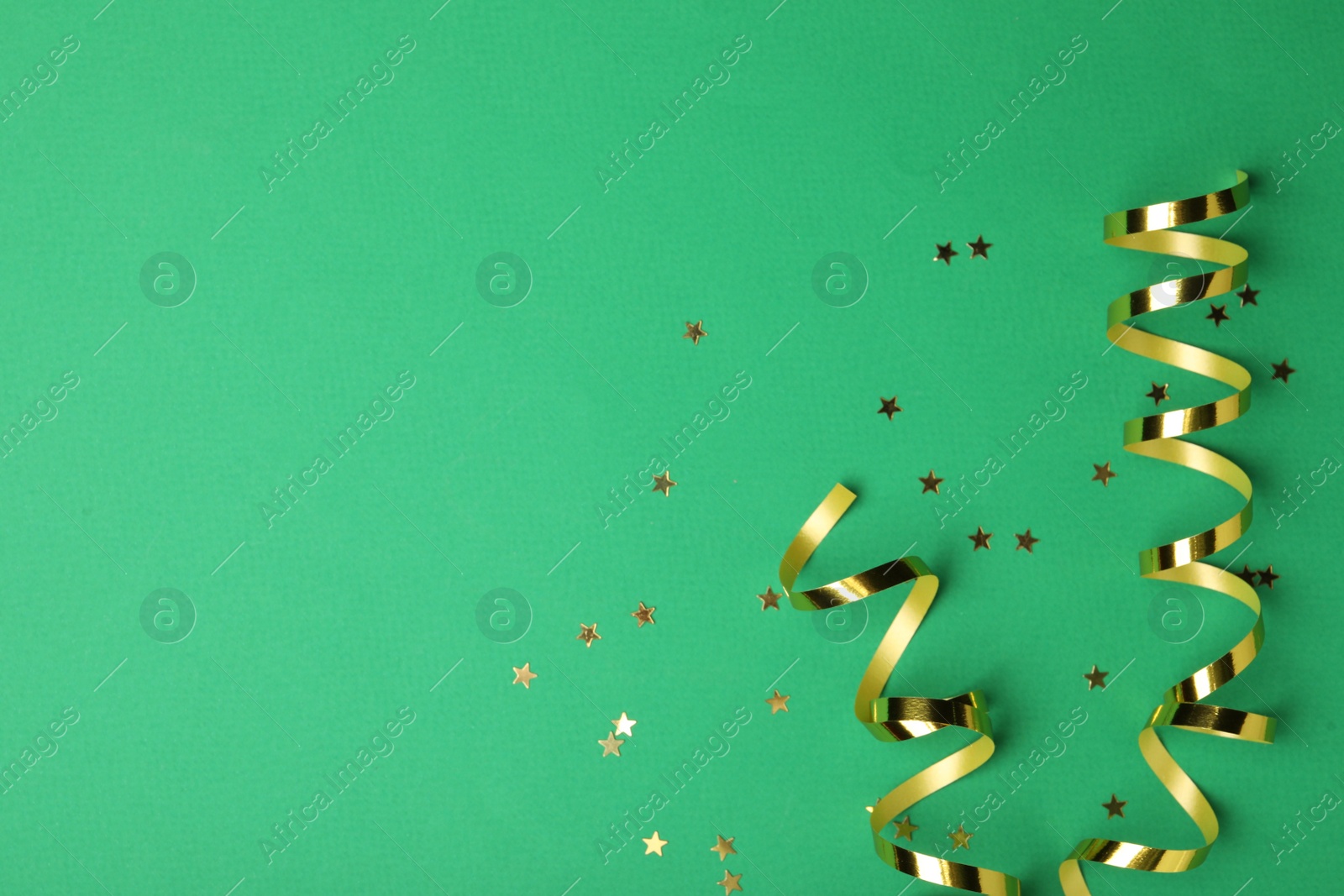 Photo of Shiny golden serpentine streamers and confetti on green background, flat lay. Space for text