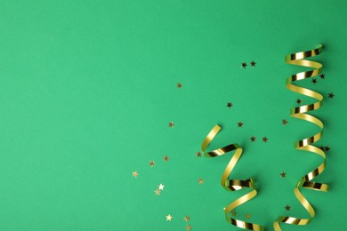 Photo of Shiny golden serpentine streamers and confetti on green background, flat lay. Space for text