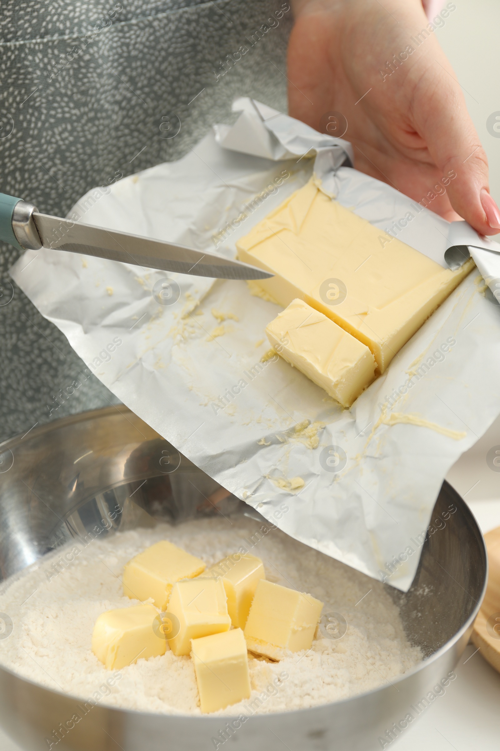 Photo of Woman adding fresh butter into bowl with flour at white table, closeup