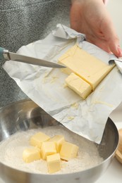 Photo of Woman adding fresh butter into bowl with flour at white table, closeup