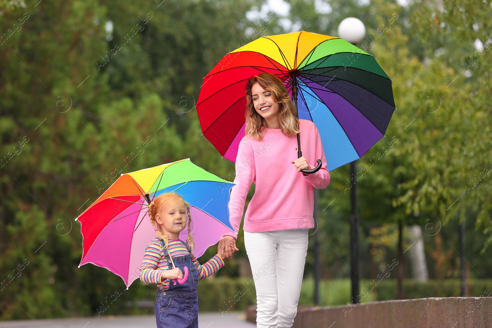 Photo of Happy mother and daughter with bright umbrellas walking in park