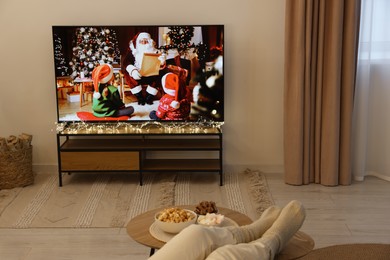Photo of Woman watching Christmas movie via TV set in room, closeup