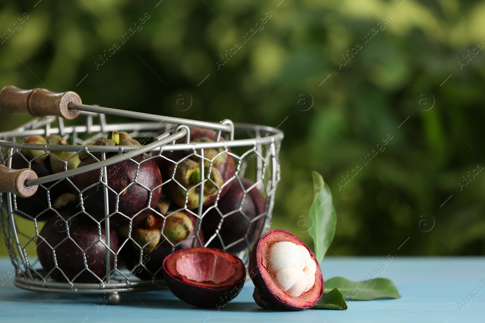 Photo of Delicious tropical mangosteen fruits on light blue table. Space for text