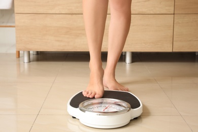 Photo of Woman stepping on floor scales in bathroom. Overweight problem