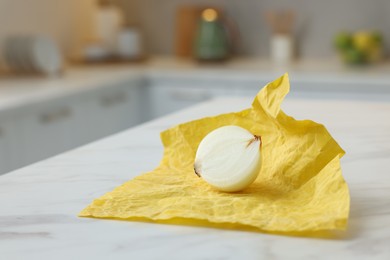 Photo of Half of onion with yellow beeswax food wrap on white table, space for text