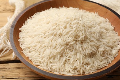 Photo of Raw basmati rice in bowl on wooden table, closeup