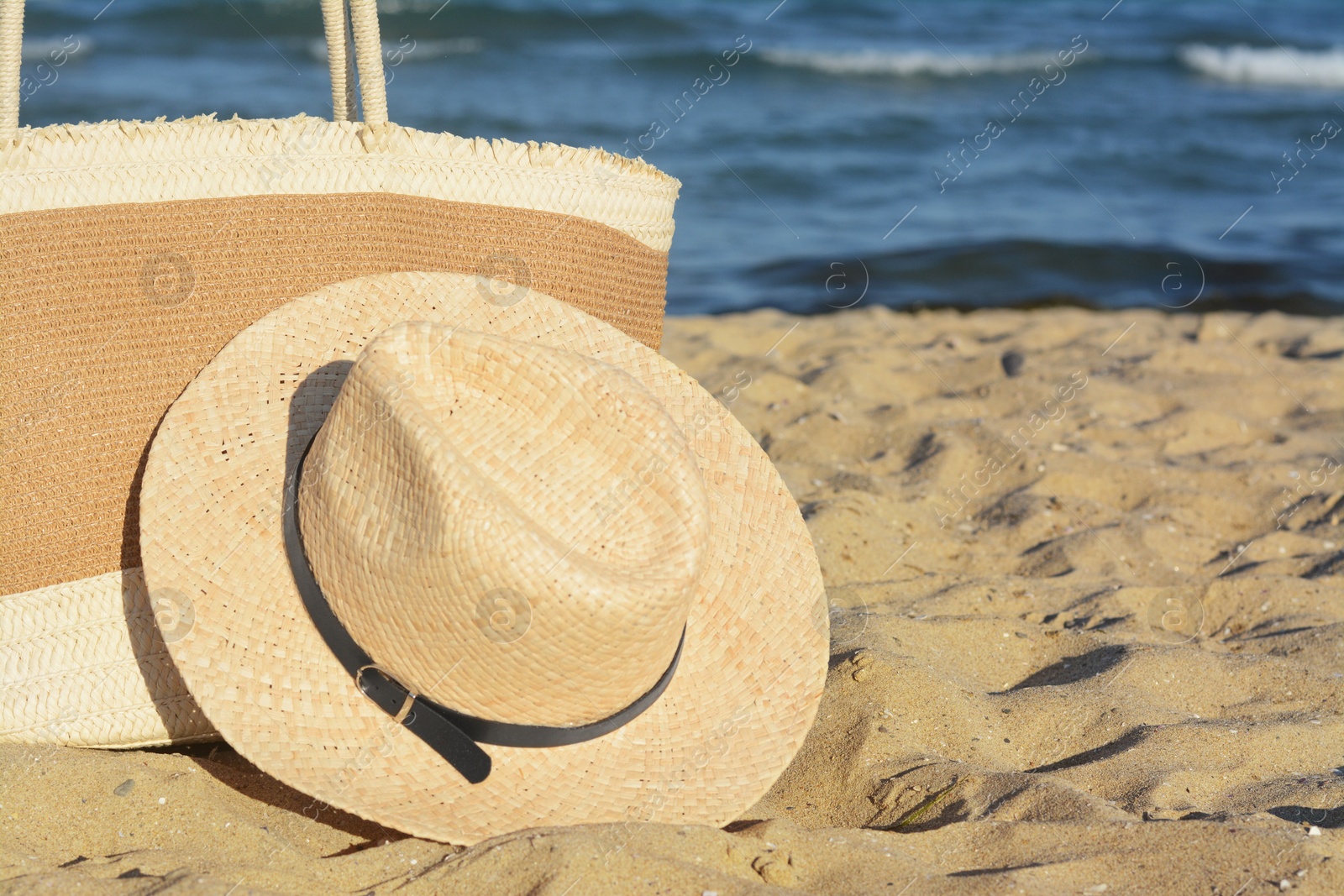 Photo of Stylish bag and hat near sea on sunny day, space for text. Beach accessories