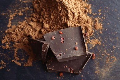 Photo of Pieces of delicious dark chocolate and cocoa powder on table