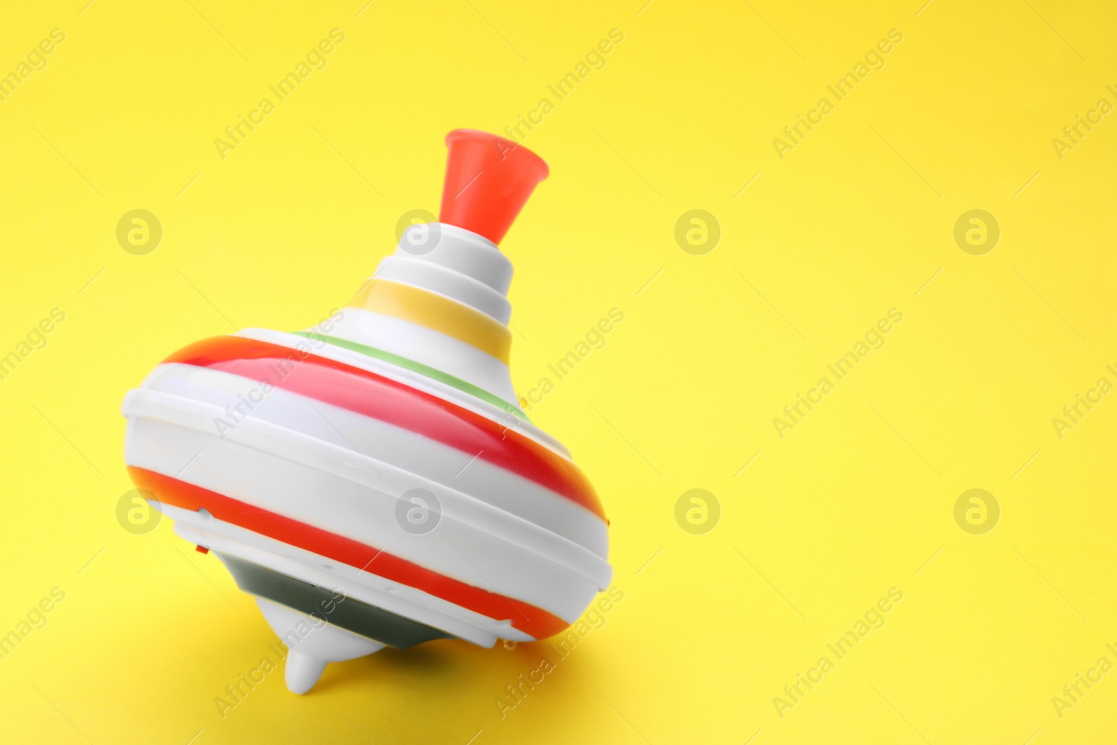 Photo of One bright spinning top on yellow background, closeup with space for text. Toy whirligig