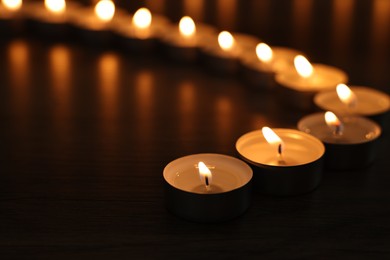 Burning candles on wooden table in darkness, closeup. Space for text