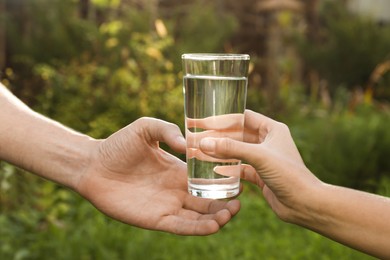 Photo of Woman giving glass of fresh water to man outdoors, closeup