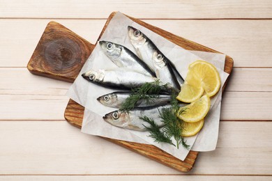 Photo of Fresh raw sprats, lemon and dill on light wooden table, top view