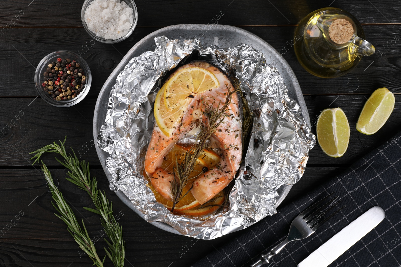 Photo of Tasty salmon baked in foil with lemon, spices and rosemary served on dark wooden table, flat lay