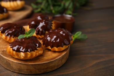 Photo of Delicious profiteroles with chocolate spread and mint on wooden table, closeup. Space for text