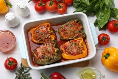 Photo of Tasty stuffed peppers in dish and ingredients on white tiled table, flat lay