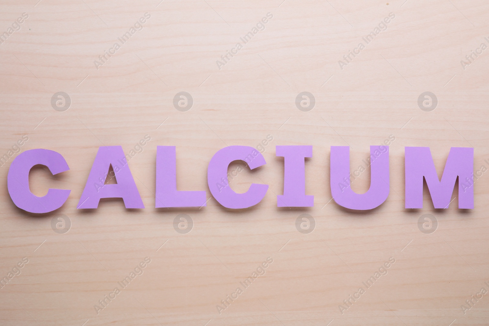 Photo of Word Calcium made of violet paper letters on wooden table, top view