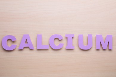 Photo of Word Calcium made of violet paper letters on wooden table, top view