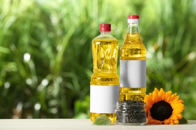 Photo of Bottles of sunflower cooking oil, seeds and yellow flower on white wooden table outdoors, space for text