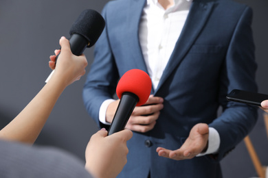 Photo of Professional journalists interviewing businessman on grey background, closeup