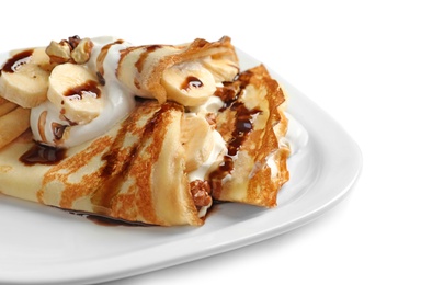 Photo of Thin pancakes with chocolate syrup, cream and banana on plate against white background