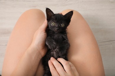 Woman with cute black kitten indoors, top view