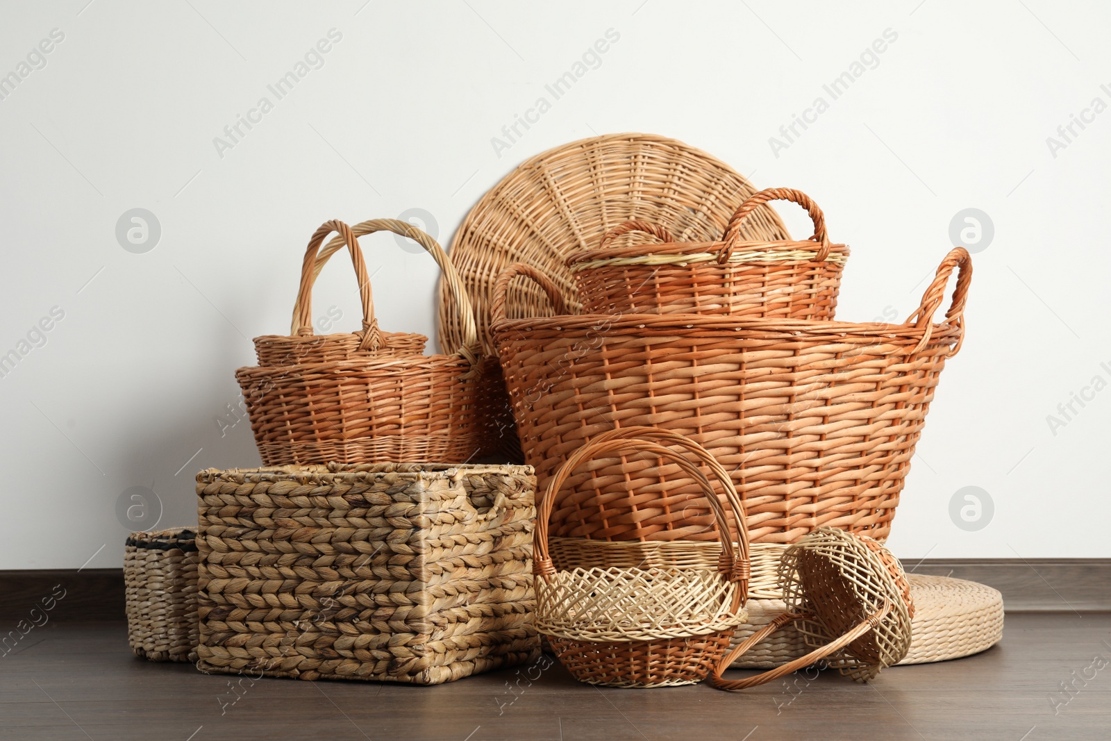 Photo of Many different wicker baskets made of natural material on floor near light wall