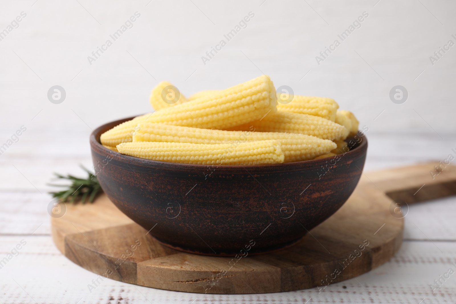 Photo of Tasty fresh yellow baby corns in bowl on white wooden table