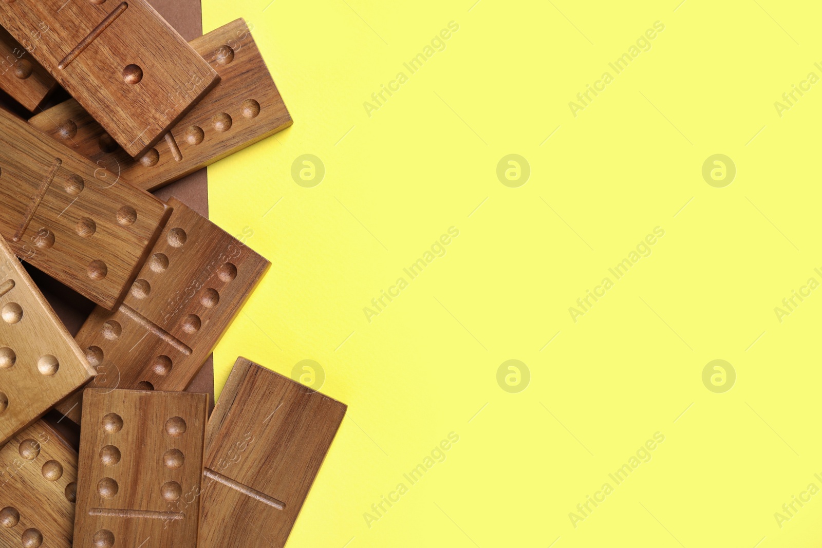 Photo of Wooden domino tiles on yellow background, flat lay. Space for text