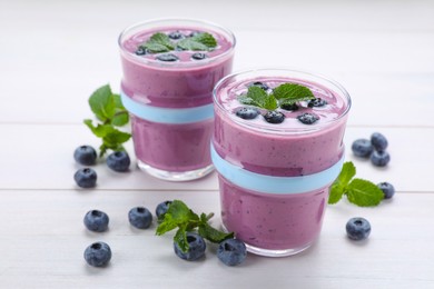 Photo of Glasses of blueberry smoothie with mint and fresh berries on white wooden table