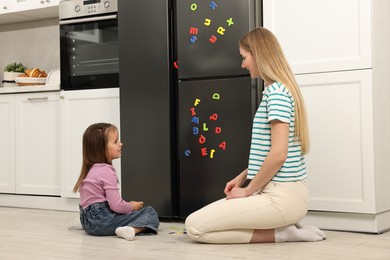 Photo of Mom and daughter putting magnetic letters on fridge at home. Learning alphabet