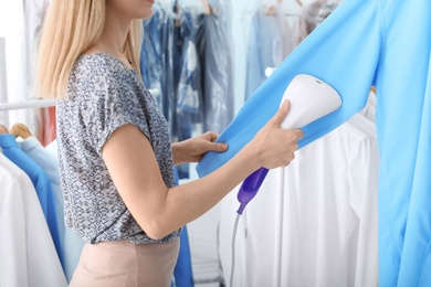 Photo of Young woman steaming shirt at dry-cleaner's