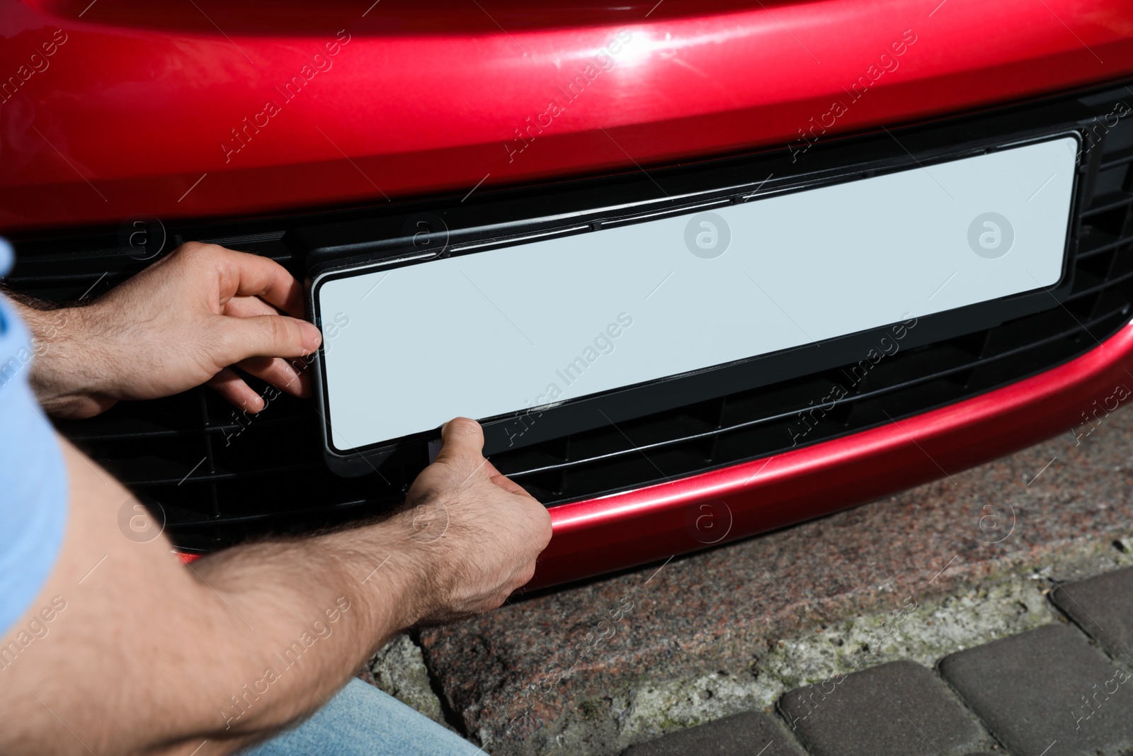 Photo of Man installing vehicle registration plate outdoors, closeup