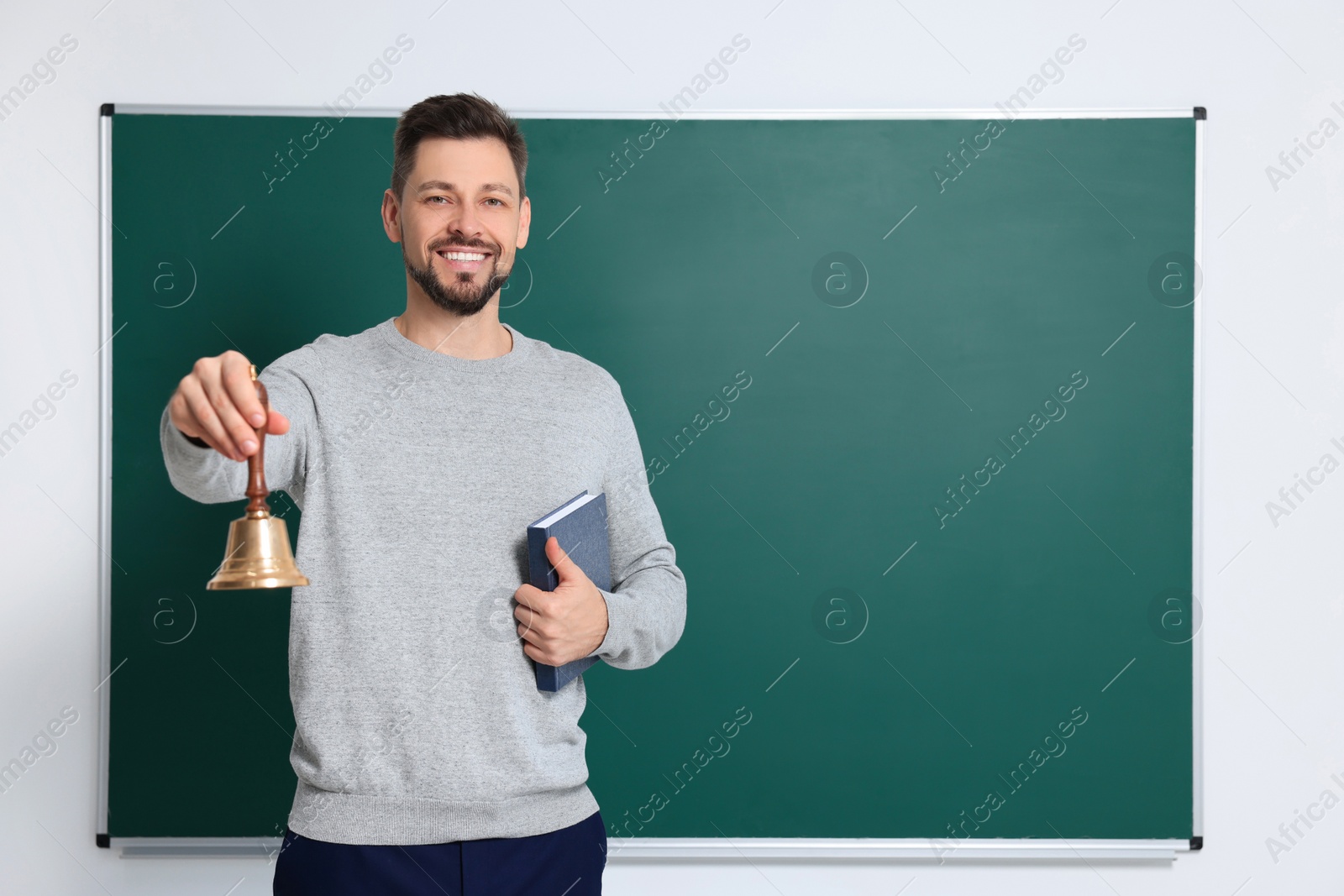 Photo of Teacher with school bell near chalkboard indoors. Space for text