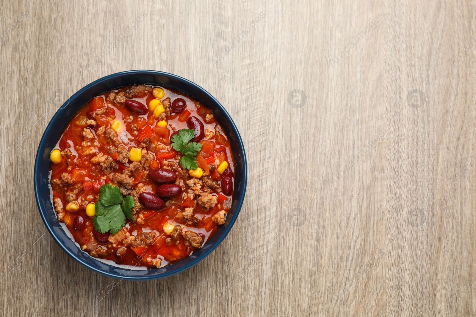 Photo of Bowl with tasty chili con carne on wooden table, top view. Space for text