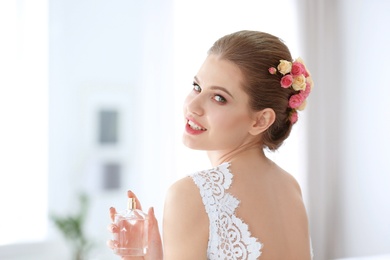 Beautiful young bride with bottle of perfume on blurred background