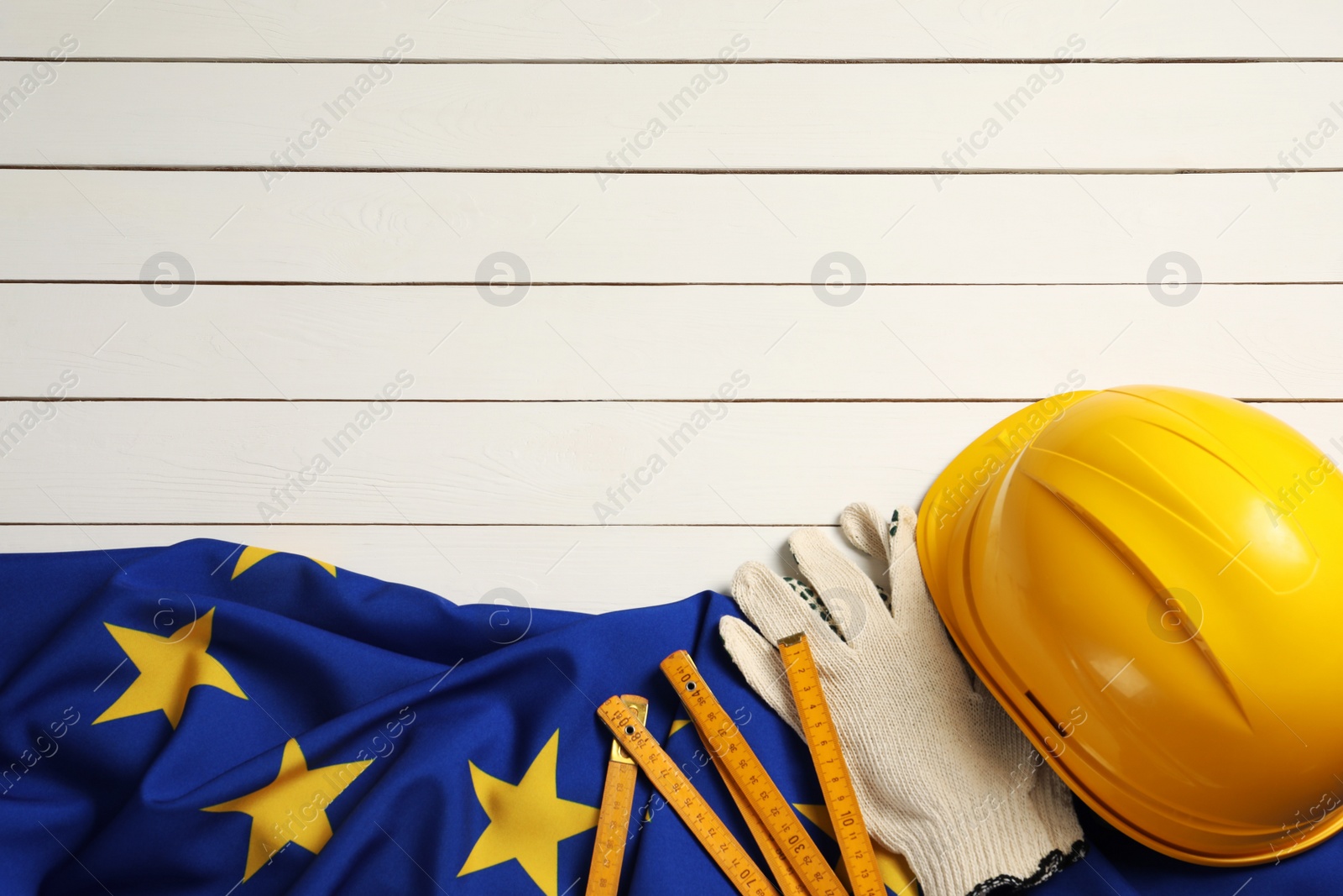 Photo of Construction tools and flag of European Union on wooden white table, flat lay. Space for text