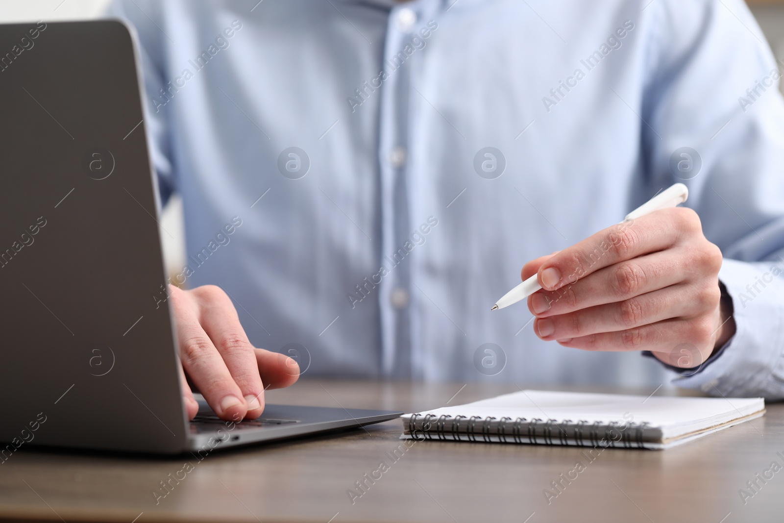 Photo of E-learning. Man taking notes during online lesson at table indoors, closeup