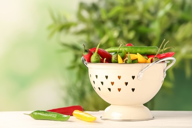 Photo of Colander with chili peppers on table against blurred background