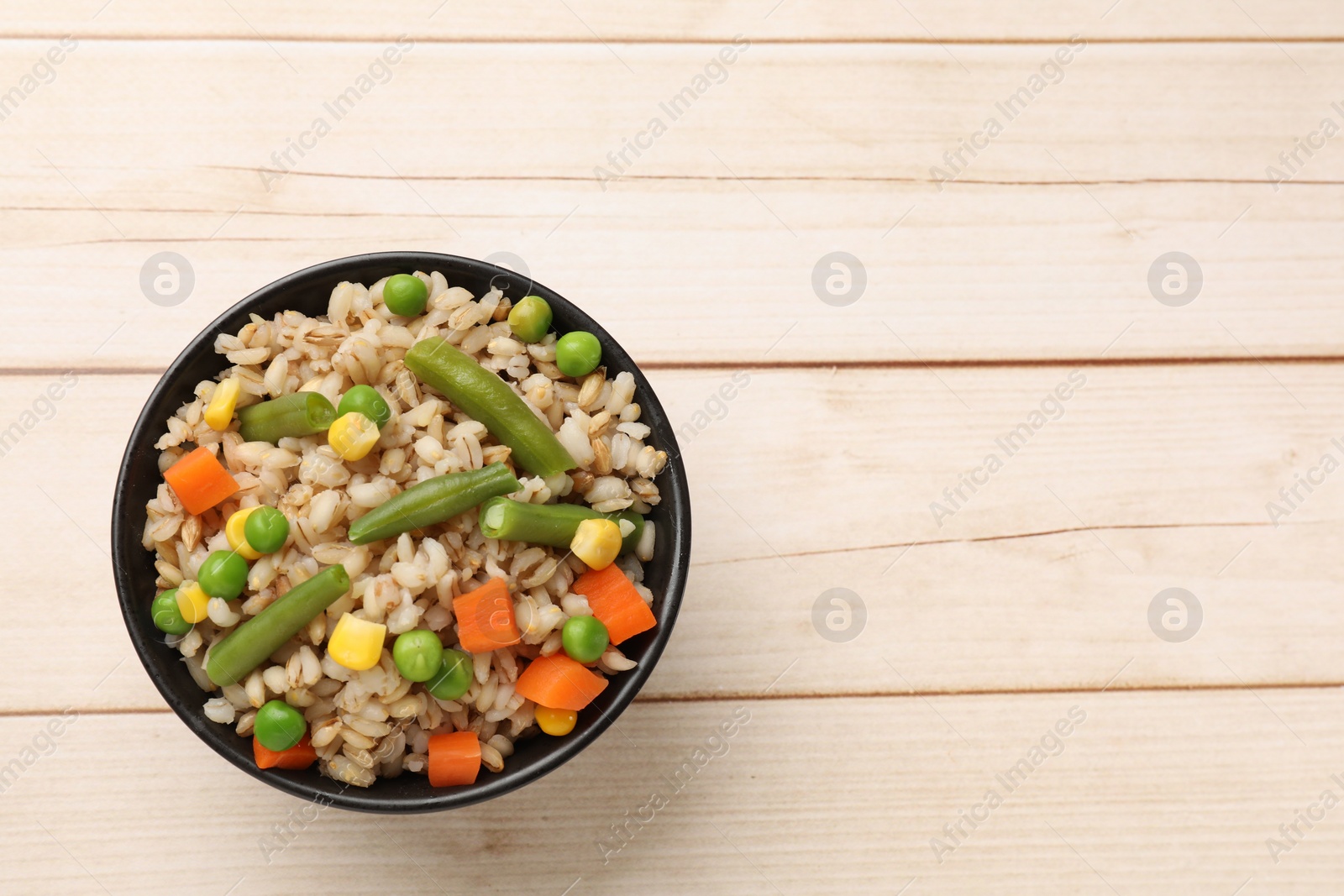 Photo of Delicious pearl barley with vegetables in bowl on wooden table, top view. Space for text