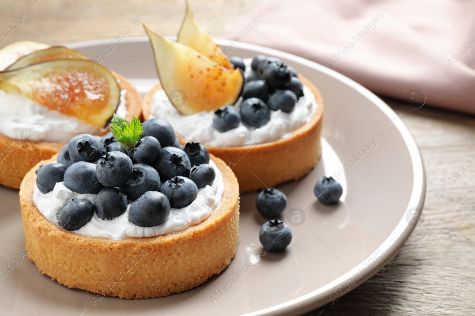 Photo of Plate of tarts with blueberries and figs on wooden table, closeup. Delicious pastries