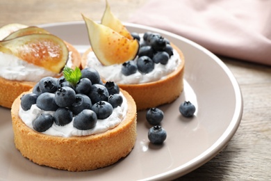 Photo of Plate of tarts with blueberries and figs on wooden table, closeup. Delicious pastries