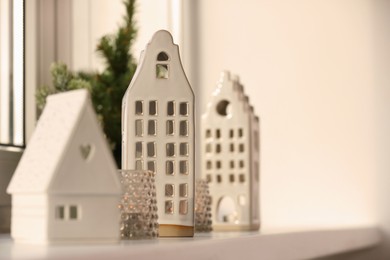 Photo of Beautiful house shaped candle holders and small fir trees on windowsill indoors, space for text
