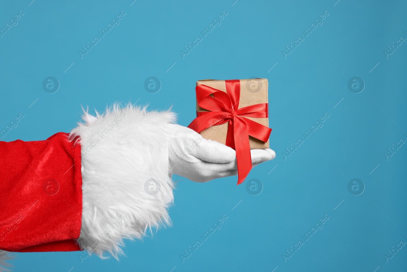 Photo of Santa Claus holding Christmas gift on light blue background, closeup
