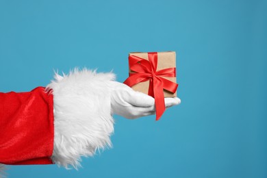 Santa Claus holding Christmas gift on light blue background, closeup