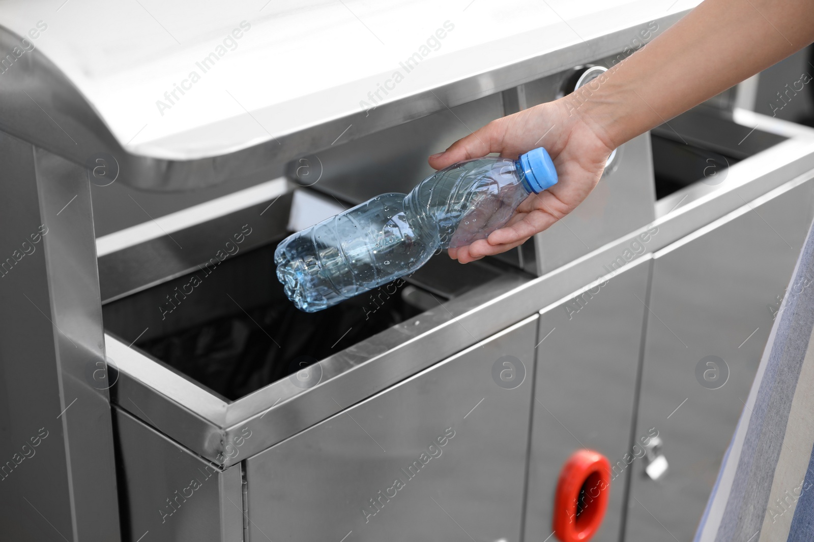 Photo of Woman throwing plastic bottle into recycling bin outdoors, closeup