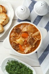 Photo of Tasty cabbage soup with meat and carrot served on white wooden table, flat lay